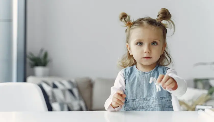 Mała dziewczynka z dwoma kucykami na głowie trzyma w ręku małą figurkę.