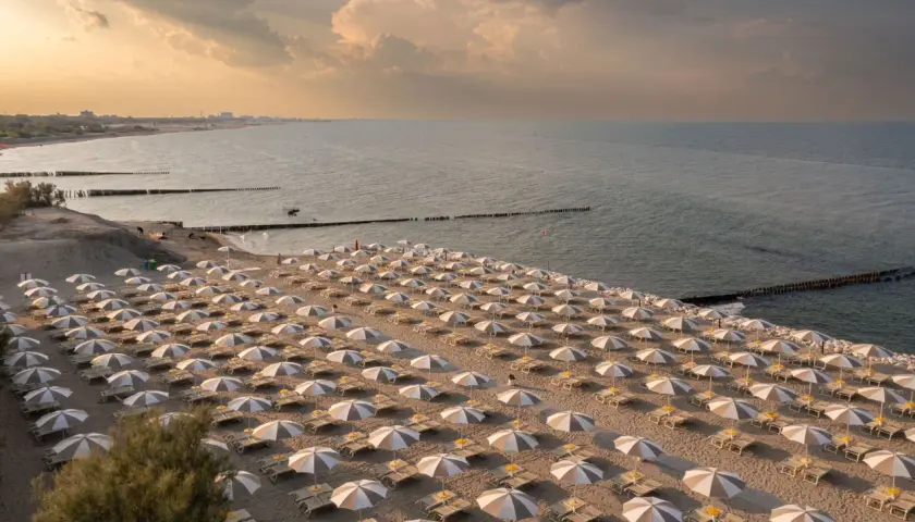 Filetto di ombrelloni e lettini sulla sabbia dorata, con il mare calmo e il cielo crepuscolare a fare da sfondo. Un'immagine che evoca la tranquillità dei **Marche mare**.