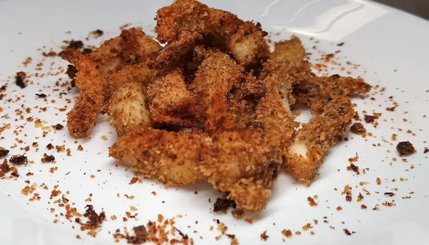 Un mucchietto di seppie gratinate al forno, dorate e croccanti, su un piatto bianco.