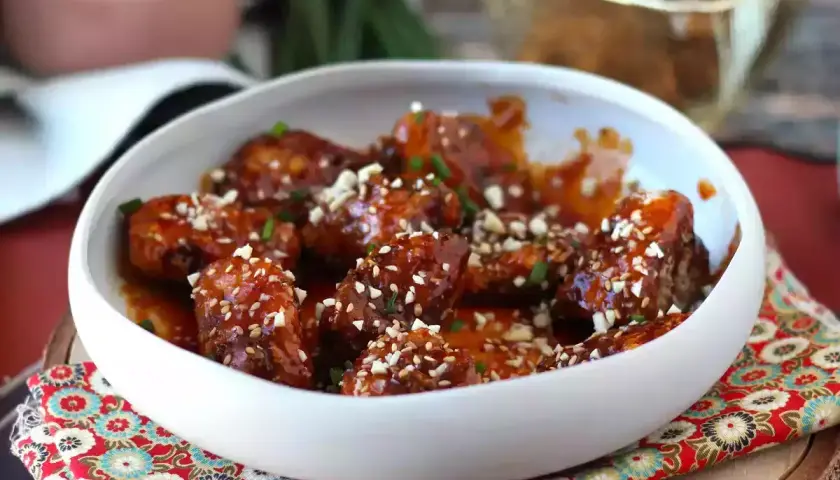 En skål med glaserad koreansk kyckling, toppad med sesamfrön och hackade nötter.