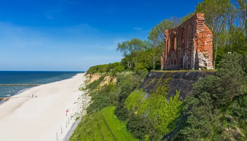 Ruiny ceglanego kościoła na klifie nad piaszczystą plażą i morzem. Idealne miejsce na weekend nad morzem.