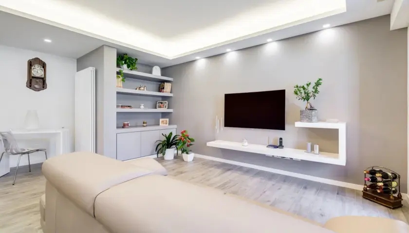 Mobile TV in cartongesso, con mensole e vani contenitori integrati. Soggiorno moderno con divano chiaro e pavimento effetto legno.