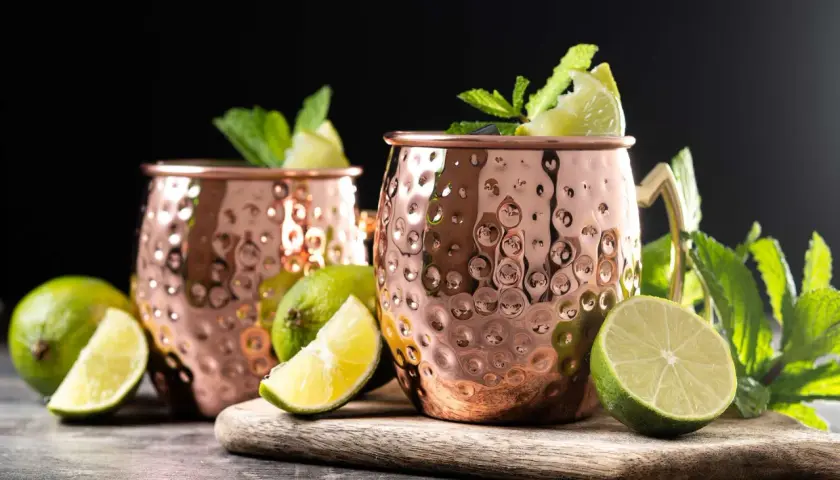 Due tazze di rame martellato per un Moscow Mule, guarnite con menta fresca e spicchi di lime.