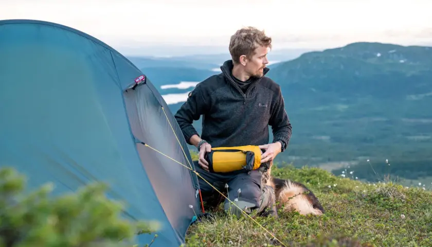 Man med hund förbereder tältet för en vintervandring i fjällen.