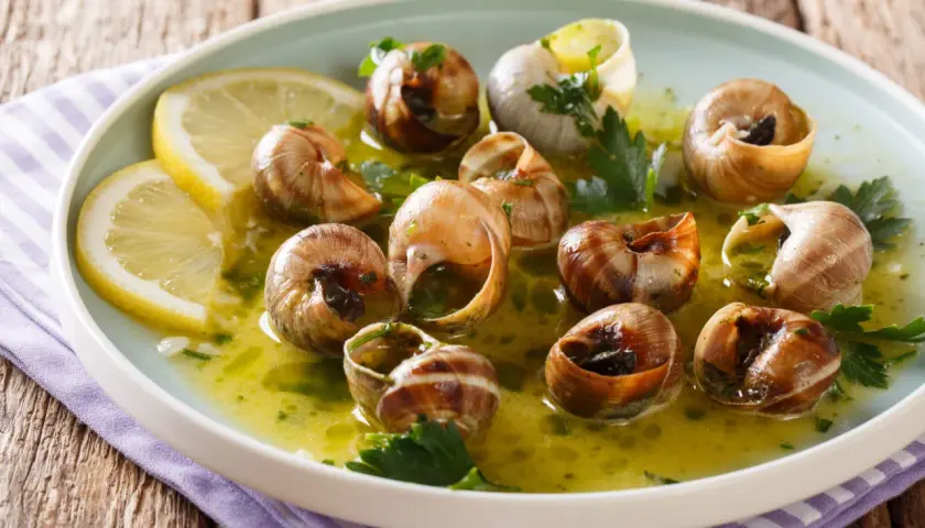 Escargot to danie z gotowanych ślimaków w sosie czosnkowo-ziołowym, podane z plasterkami cytryny.