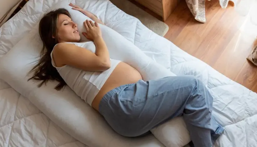 Femme enceinte dormant sur le côté, soutenue par un coussin, cherchant le confort pour éviter la remontée acide grossesse nuit.