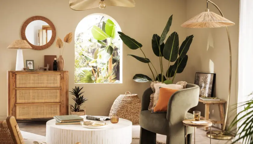 Salon bohème avec meubles en rotin et touches dorées. Le vert du fauteuil et l'orange du coussin s'accordent bien avec le doré.
