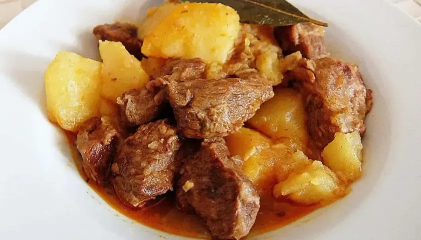 Sabroso morcillo de ternera guisado con patatas y una hoja de laurel, servido en un plato blanco.