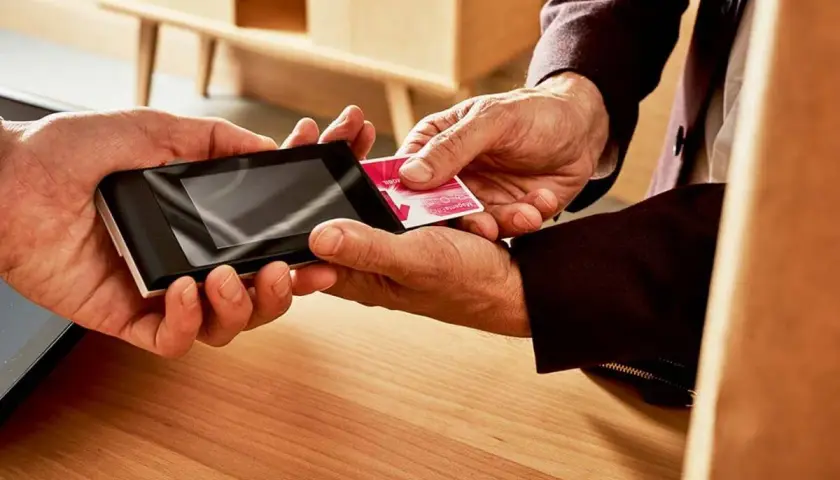 Dwie dłonie zbliżają kartę do terminala płatniczego. To prosty sposób, jak doładować telefon na kartę.