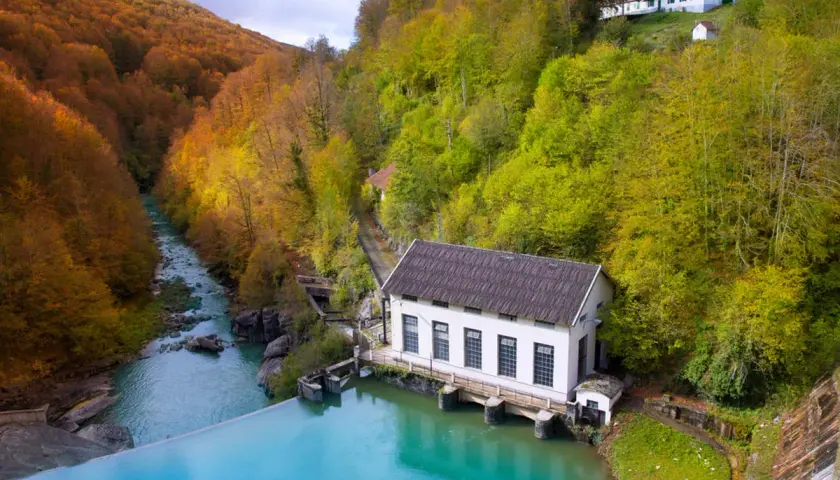 Embalse de agua turquesa junto a una central eléctrica, rodeado de bosques otoñales. Ideal para rutas selva de Irati.
