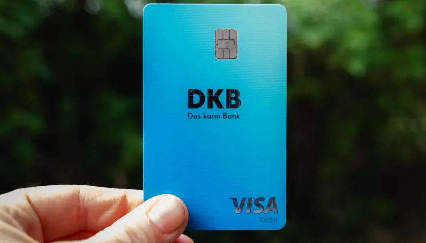 Eine blaue DKB Visa Debitkarte wird in der Hand gehalten, mit unscharfem Grün im Hintergrund.