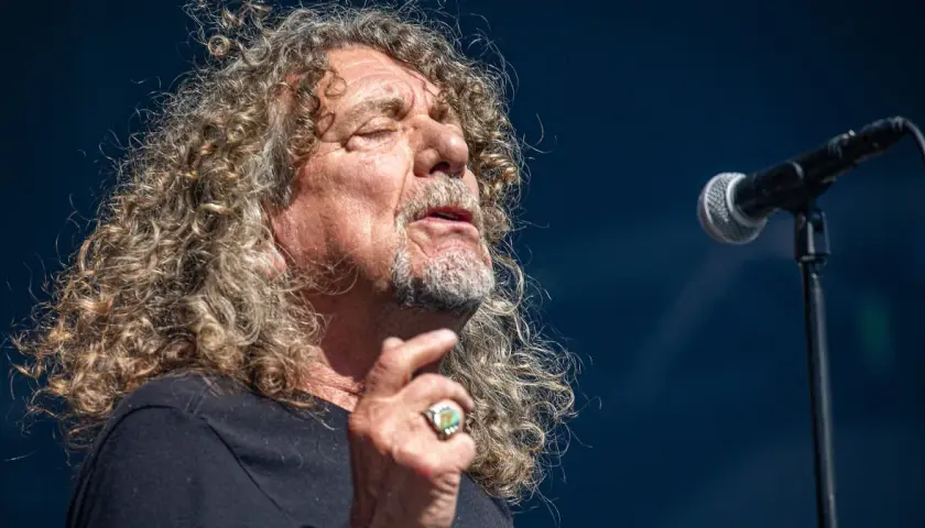 Wokalista Led Zeppelin, Robert Plant, śpiewa do mikrofonu, z charakterystyczną burzą kręconych włosów.