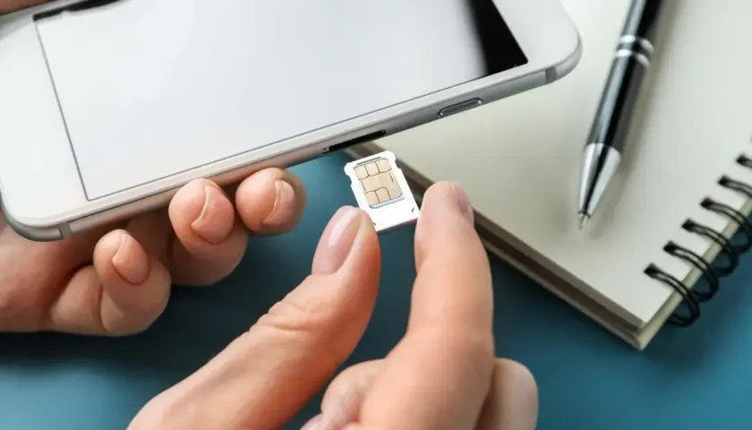 Dłoń wyjmuje kartę SIM z telefonu. Na biurku leży notatnik i długopis. To ważny numer na kartę.