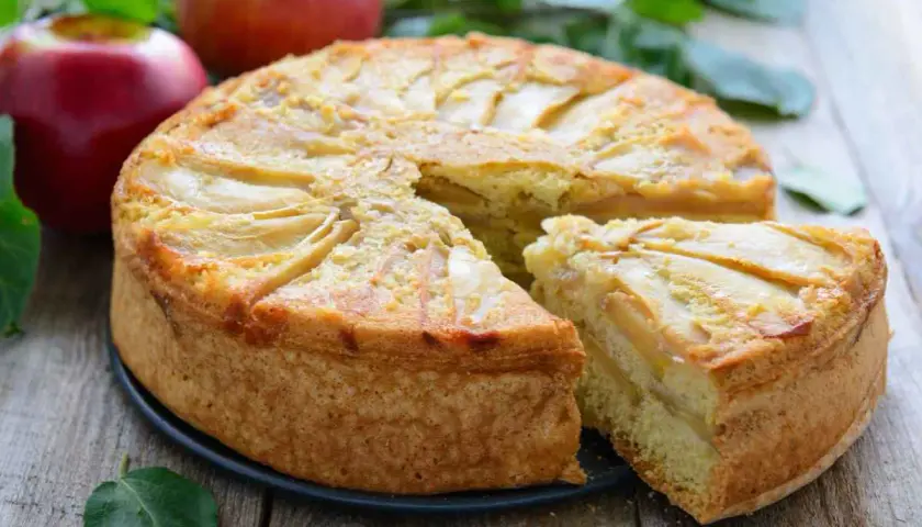 Deliziosa torta di mele vegana con fette di mela disposte a raggiera sulla superficie dorata. Una fetta è già stata servita.
