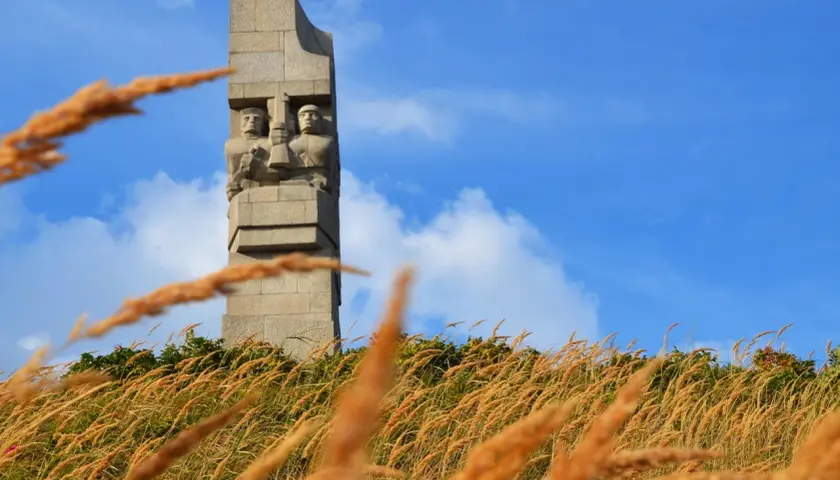 Pomnik Obrońców Wybrzeża na Westerplatte podczas zwiedzania. W oddali widać dwie kamienne postacie żołnierzy.