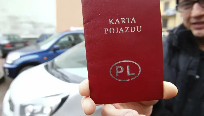 Czerwona karta pojazdu z napisem "KARTA POJAZDU" i symbolem "PL" w owalu, trzymana przed białym samochodem.