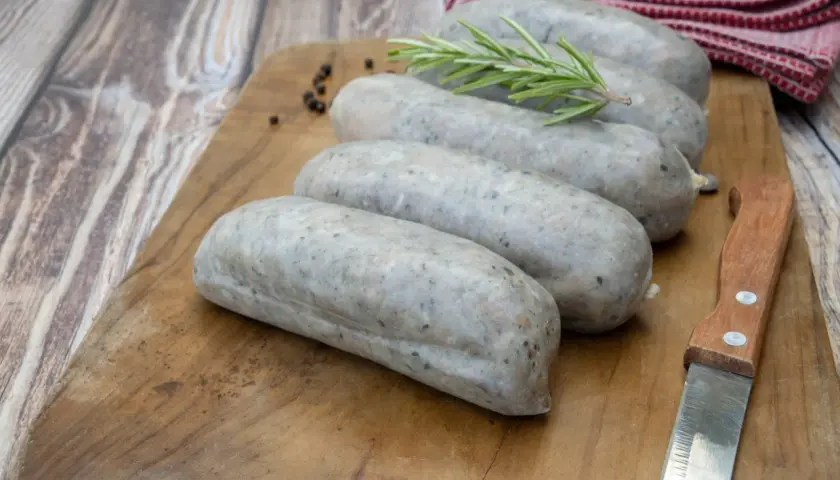 Saucisses grises sur planche en bois, avec romarin et poivre. La différence entre andouille et andouillette est subtile, mais la texture ici suggère une andouillette.