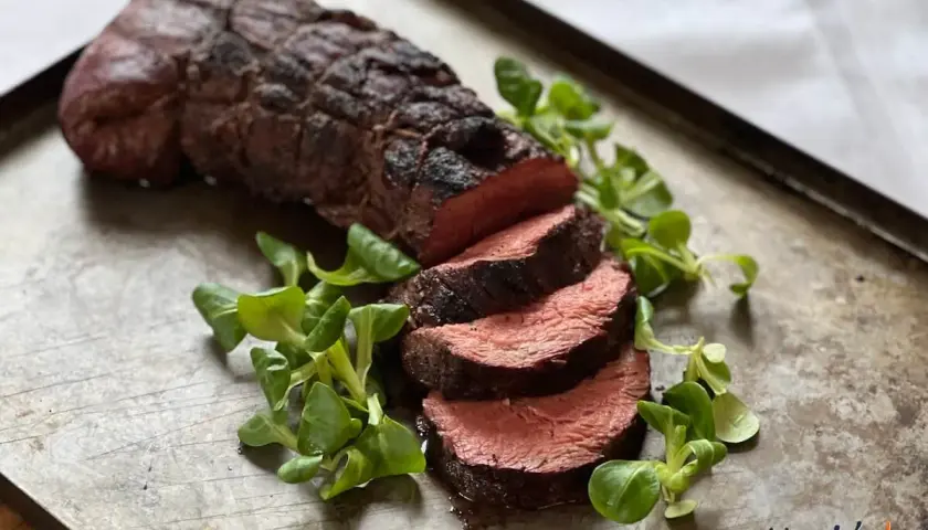 Perfekt grillad oxfilé, saftig och röd i mitten, serverad med färska gröna blad på en rustik plåt. En riktig höjdare för grillmästaren!