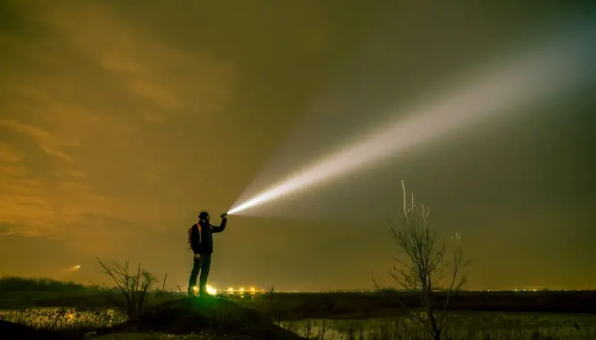 Mężczyzna z plecakiem oświetla nocne niebo potężnym snopem światła z latarki o dużym zasięgu.