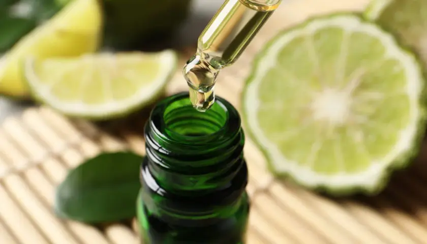 Une goutte d'huile essentielle de bergamote tombe d'une pipette dans un flacon vert. Un remède de grand-mère pour lutter contre la fatigue, entouré de fruits coupés.
