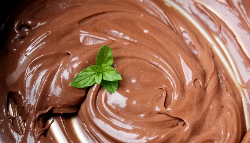 Una fogliolina di menta fresca adorna una spirale di lucida ganache al cioccolato, invitando a un assaggio goloso.
