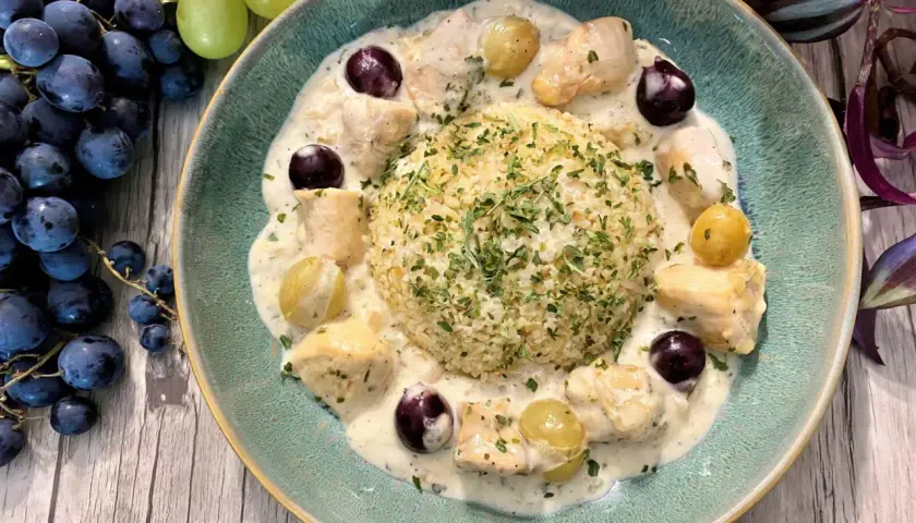 Un délicieux poulet au raisin crémeux, servi avec du riz et garni de persil frais. Des grappes de raisins noirs et verts complètent cette assiette appétissante.