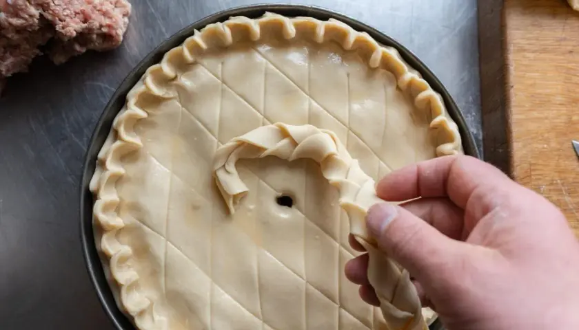 Préparation d'une tarte salée, peut-être une recette joue de porc rapide. Une pâte est décorée avec une tresse.
