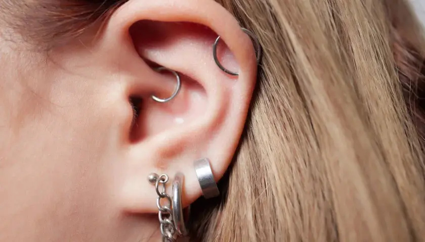 Ucho z kilkoma kolczykami, w tym daith piercing z małym kółkiem.