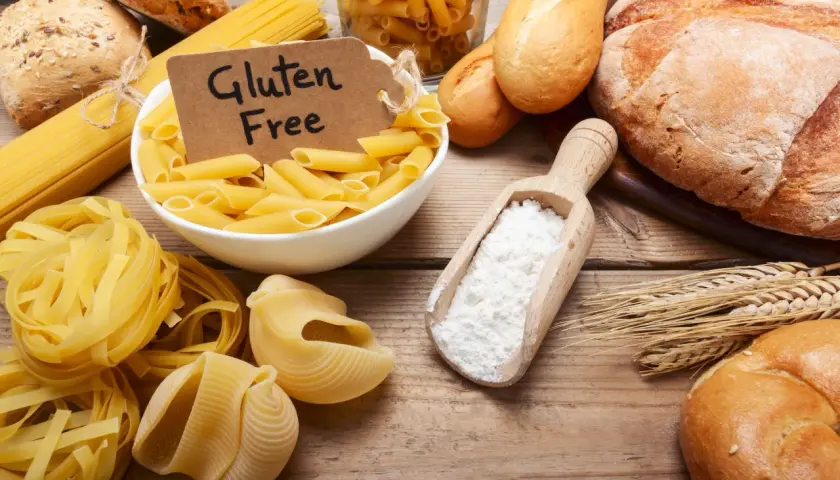 Różne rodzaje makaronów i pieczywa, a także mąka i kłosy zbóż. Etykieta "Gluten Free" sugeruje dyskusję: czy gluten jest zdrowy?