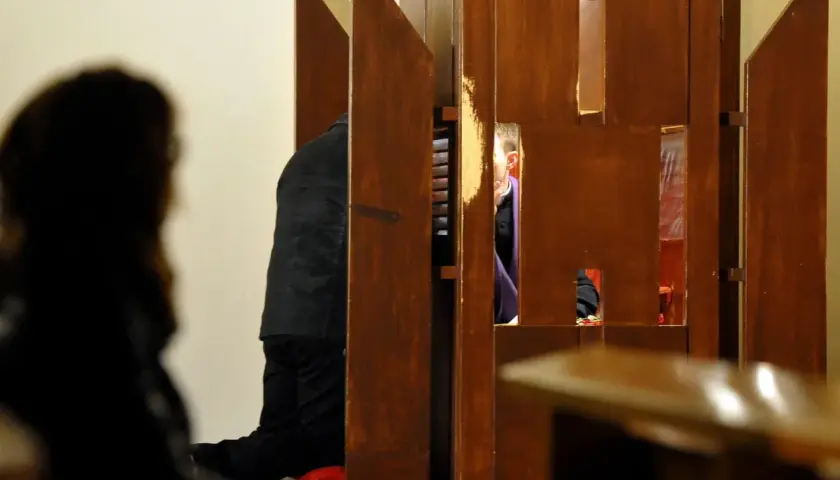 W konfesjonale klęczy mężczyzna, a za kratkami widać księdza. Czy konieczna jest spowiedź przed chrztem?