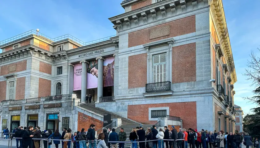 Kolejka turystów przed wejściem do Muzeum Prado w Madrycie. Monumentalna fasada budynku z cegły i kamienia ozdobiona jest banerami wystawowymi.
