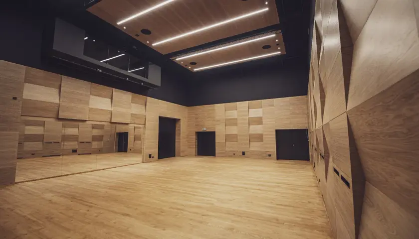 Nowoczesna sala prób w Teatrze Ludowym w Krakowie. Drewniane ściany i podłoga, lustra i oświetlenie tworzą inspirującą przestrzeń.