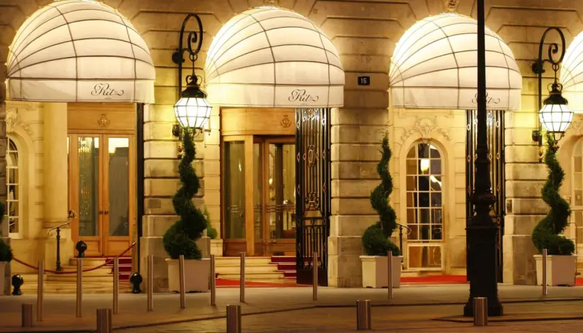 Eleganckie wejście do słynnego paryskiego hotelu Ritz, oświetlone latarniami i ozdobione spiralnymi drzewkami.