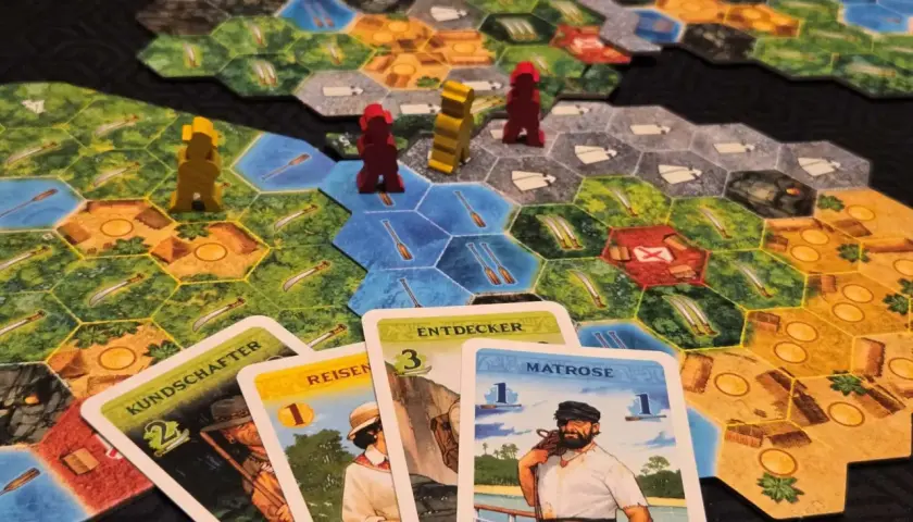 Spielbrett mit Figuren und Karten. Ein Seemann, Entdecker und andere Charaktere sind auf den Karten abgebildet. Ein spannendes Spiel für alle, die gute Brettspiele lieben.