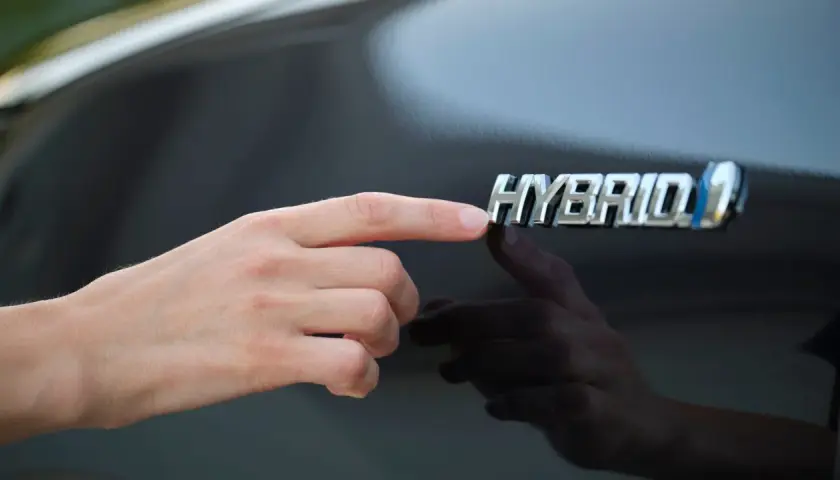 Dłoń dotyka znaczka "HYBRID", symbolizując rozważania nad silnik hybrydowy wady i zalety.