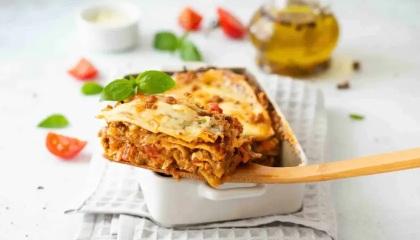 Une part généreuse de lasagne, digne d'une recette de chef italien, est servie. Tomates et basilic frais décorent ce plat réconfortant.