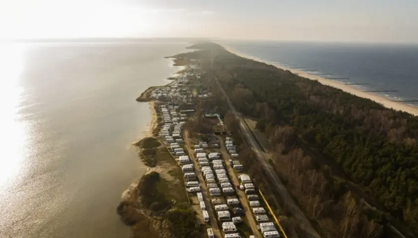 Widok z lotu ptaka na długi pas kempingów w Polsce, rozciągający się wzdłuż wybrzeża Morza Bałtyckiego i jeziora.