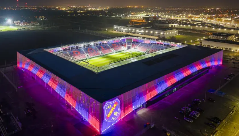 Nowoczesny stadion Odra Opole nocą, oświetlony na czerwono i niebiesko.