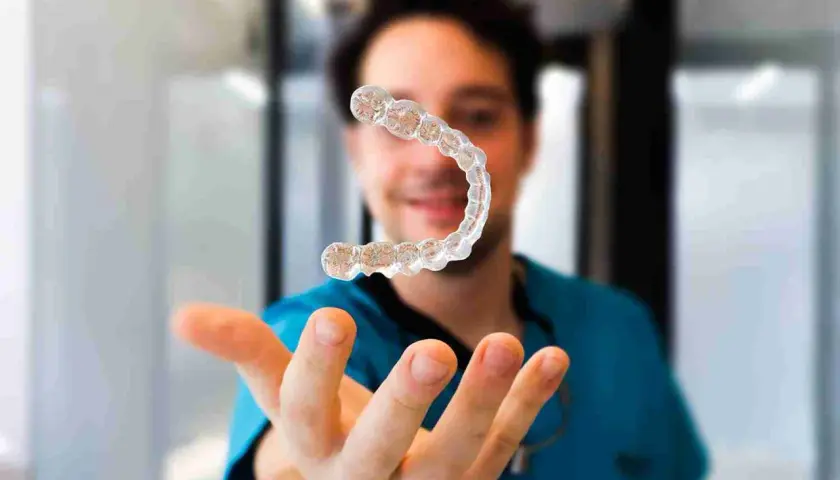 Un dentista sonriente muestra un alineador invisible, explicando cómo funcionan los alineadores invisibles para corregir la sonrisa.