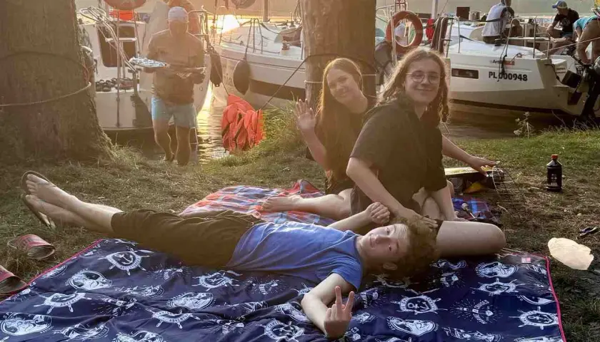 Boże Ciało w czerwcu nad jeziorem. Rodzina odpoczywa na kocu, w tle łodzie i zachód słońca.