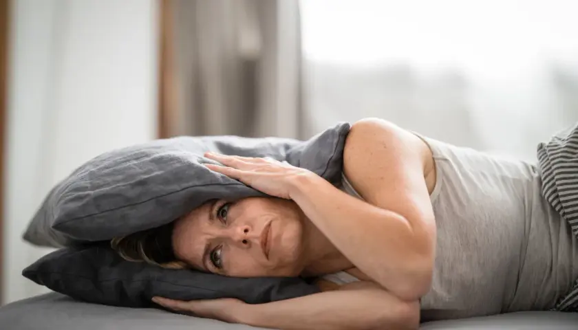 Frau mit Kissen über dem Kopf, die unter Tinnitus leidet und nach Linderung durch Osteopathie sucht.