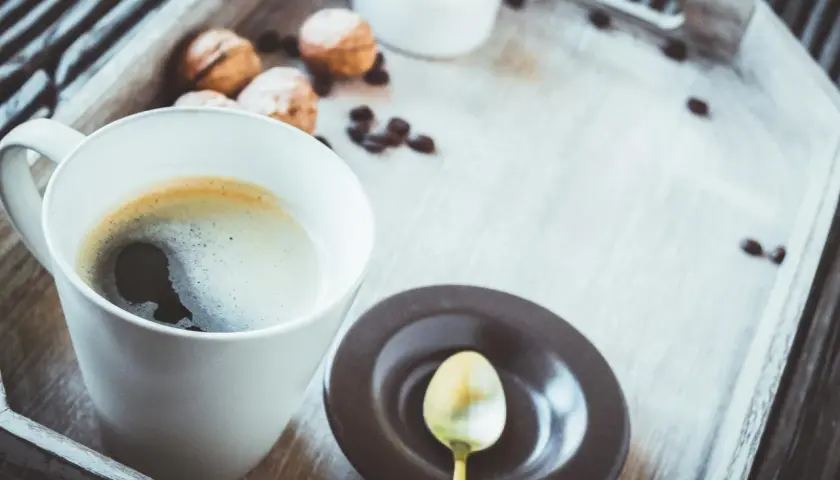 Eine Tasse schwarzer Kaffee gesund, mit Keksen und Kaffeebohnen auf einem Holzteller.