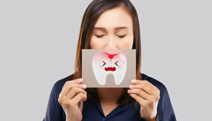 Donna con gli occhi chiusi mostra un disegno di un dente che cade, con espressione sofferente e macchie di sangue.