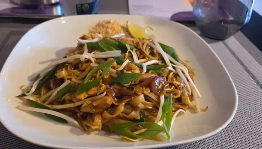 Pad thai z kurczakiem, kiełkami fasoli mung, szczypiorkiem i ćwiartką limonki na białym talerzu.