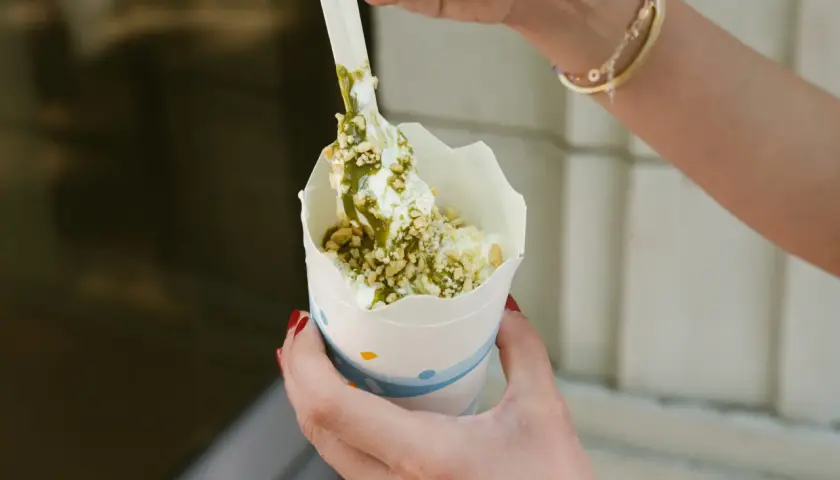 Ręce trzymają kubek z lodami mcflurry pistacjowe, posypane orzeszkami i polane zielonym sosem.