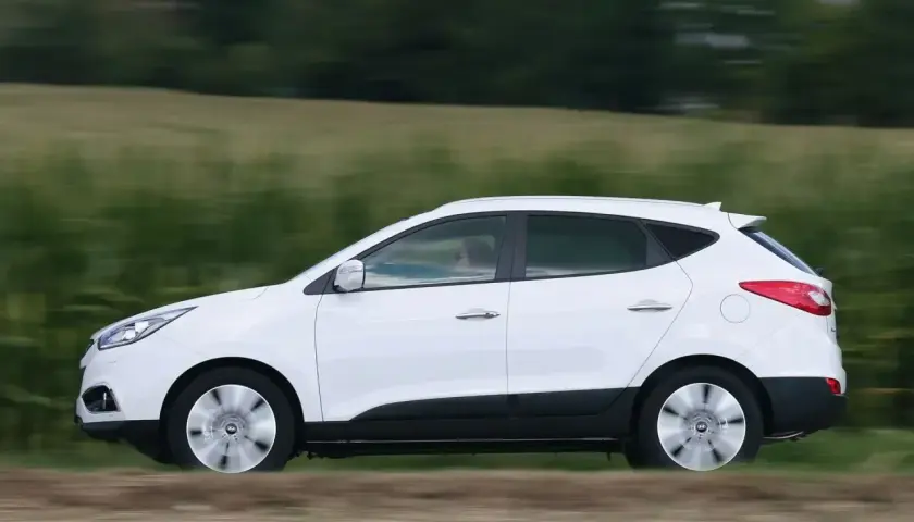 Biały Hyundai ix35 2.0 benzyna w ruchu, z rozmytym tłem zielonych pól i drzew.