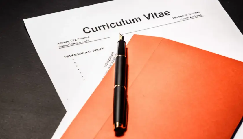 Eleganckie pióro na tle dokumentu Curriculum Vitae po angielsku i pomarańczowej koperty.