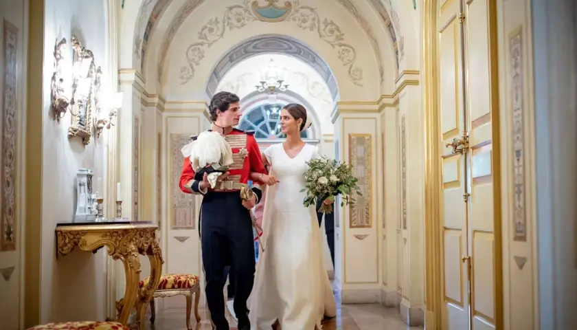 Sofía Palazuelo y su esposo, con traje de gala, caminan por un pasillo adornado, celebrando su boda.