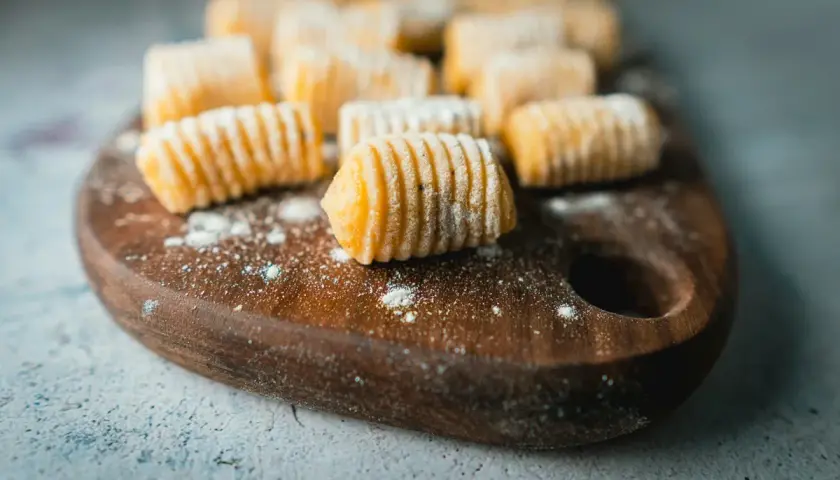 Gnocchi di patate fatti in casa, pronti per essere cucinati, disposti su un tagliere di legno scuro.