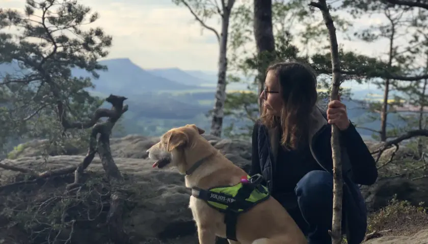 Pies i jego opiekunka podczas dog trekking w górach. Pies w kamizelce Julius-K9 patrzy w dal.
